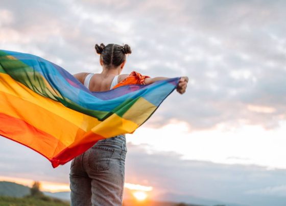 Foto colorida de mulher com bandeira do orgulho LGBT